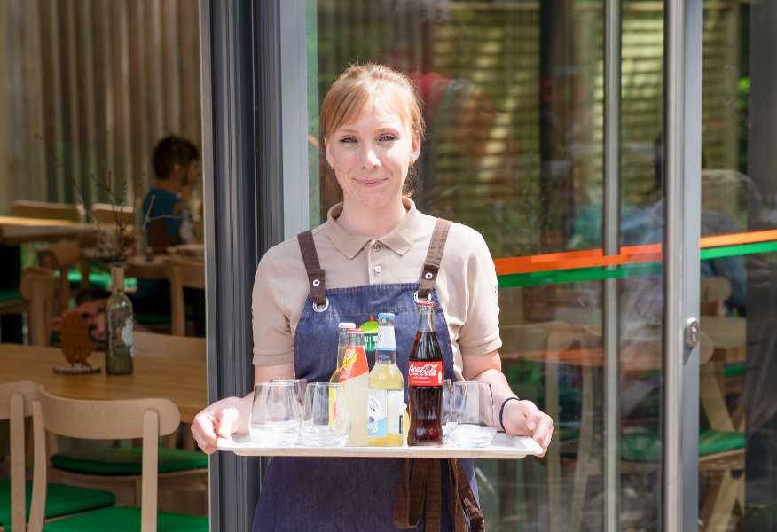 Eine Mitarbeiterin der Gastronomie serviert den Gästen auf der Terrasse des Restaurants Chez Emile frische gekühlte Getränke.