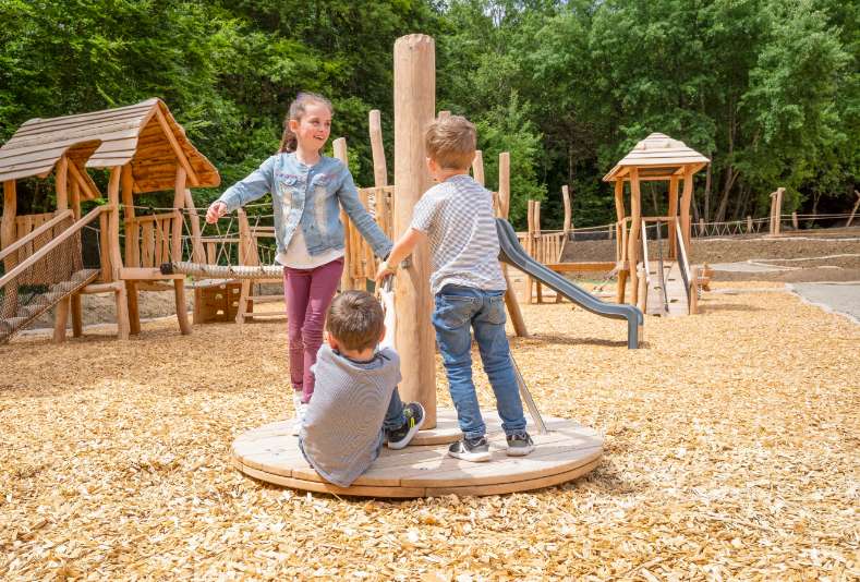 Siblings have great fun on a merry-go-round in the adventure playground Adventure Forest Alsace.