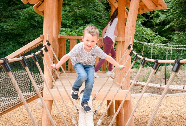 Ein Junge balanciert über ein Seil der Spielstation petit bourg im Spielplatz Abenteuerwald Elsass.