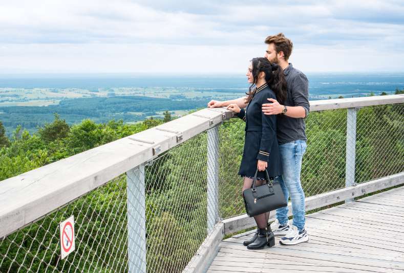 Ein Paar genießt den Ausblick auf die Rheinebene vom Aussichtsturm des Baumwipfelpfad Elsass aus.
