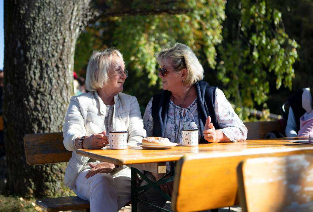 Dva senioři popíjejí kávu a pojídají zákusky po návštěvě Stezky korunami stromů v Neuschönau.
