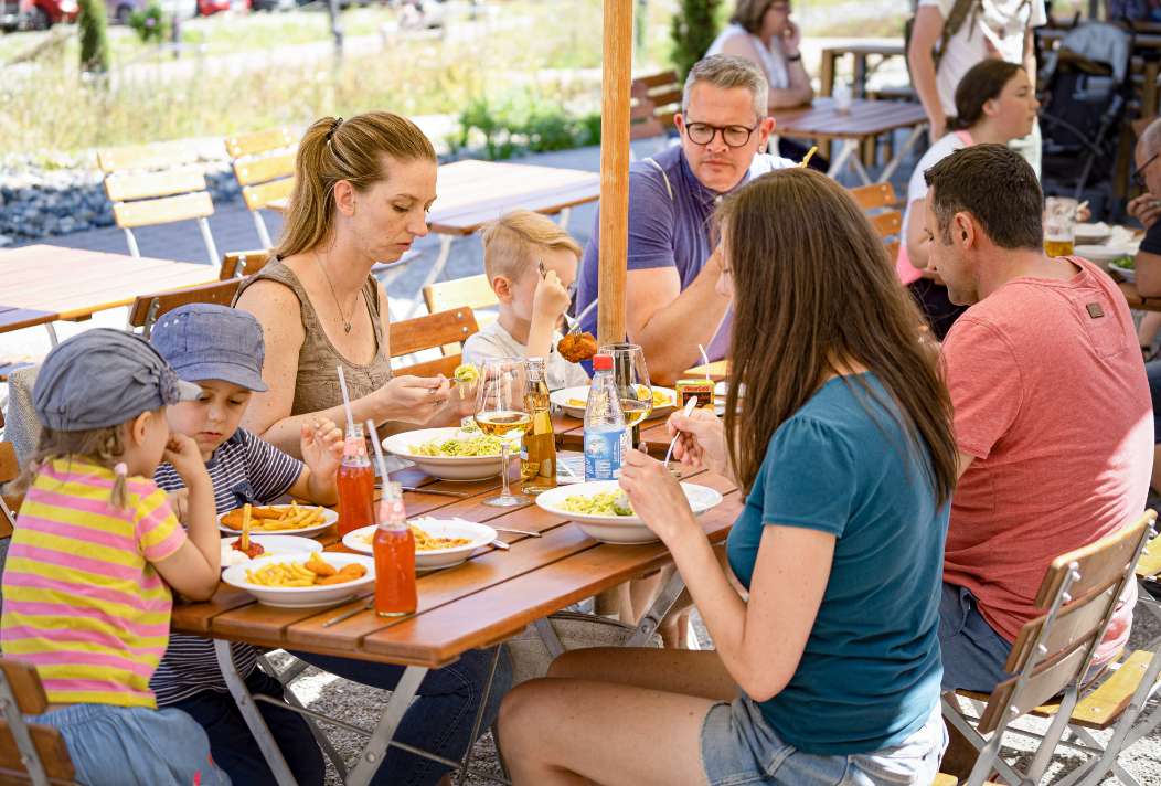 Eine Gruppe an Menschen nimmt eine Mahlzeit auf der Terrasse des Restaurants zu sich.