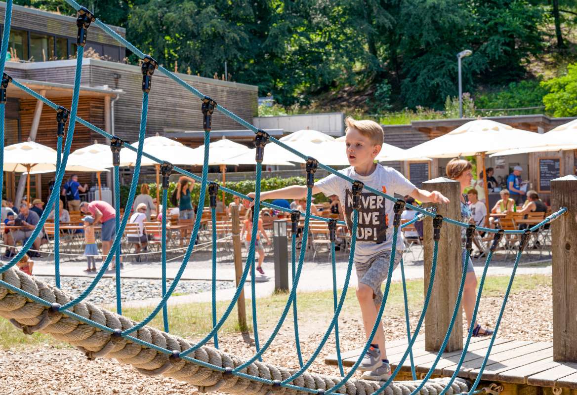 Ein Kind spielt auf dem Spielplatz mit Sichtkontakt zur Terrasse des Restaurants Boomhus im Naturerbe Zentrum Rügen.