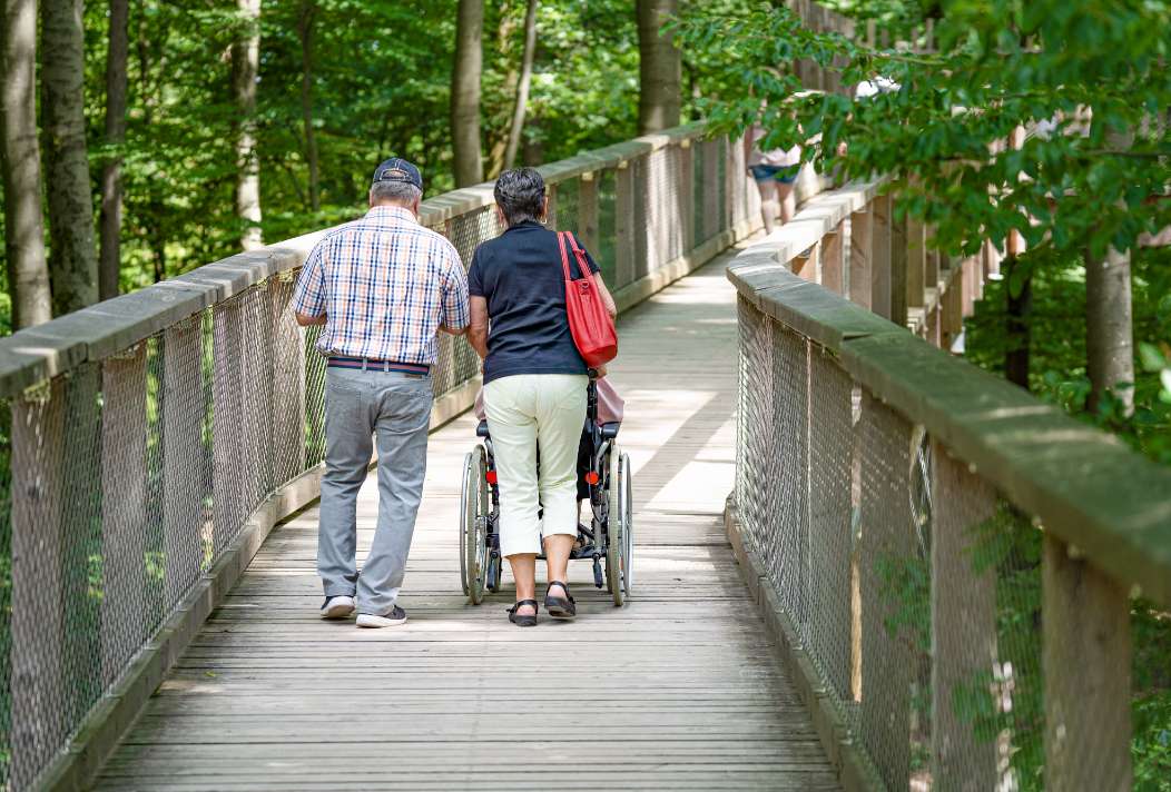 An elderly couple pushes a wheelchair user across the barrier-free Treetop Walk Saarschleife.