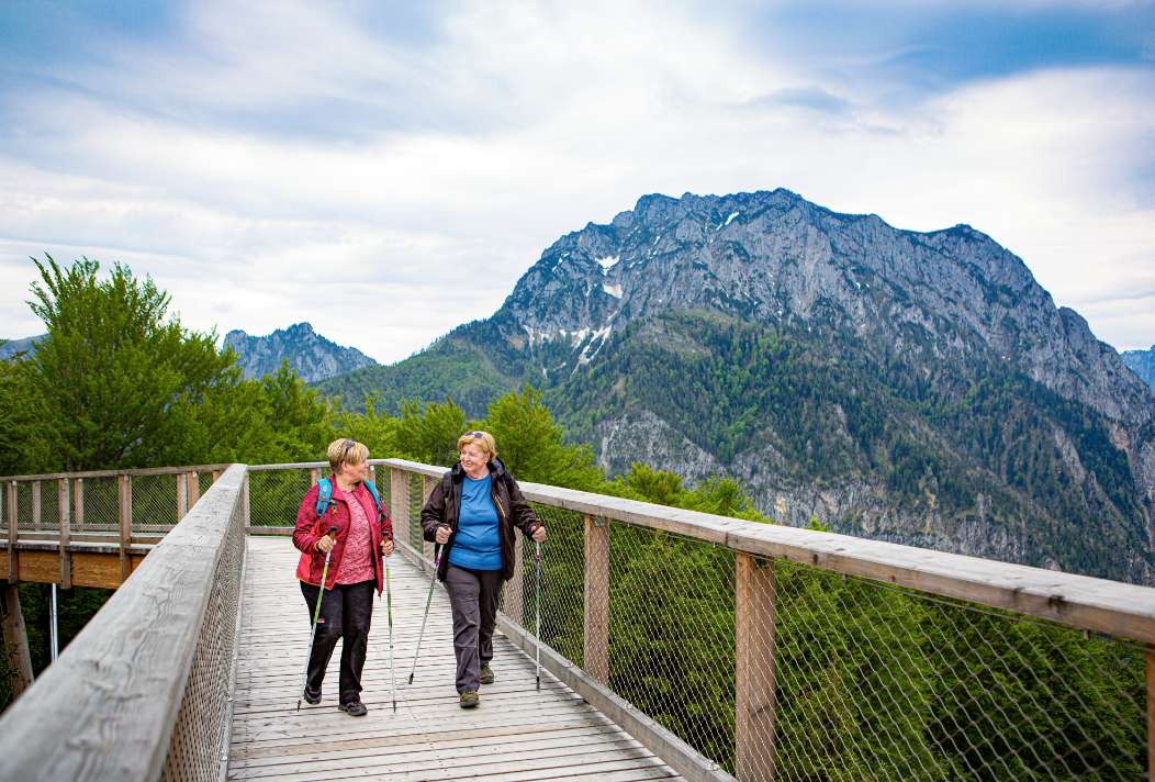 Two women are happily walking on the path, the Traunstein can be seen behind them