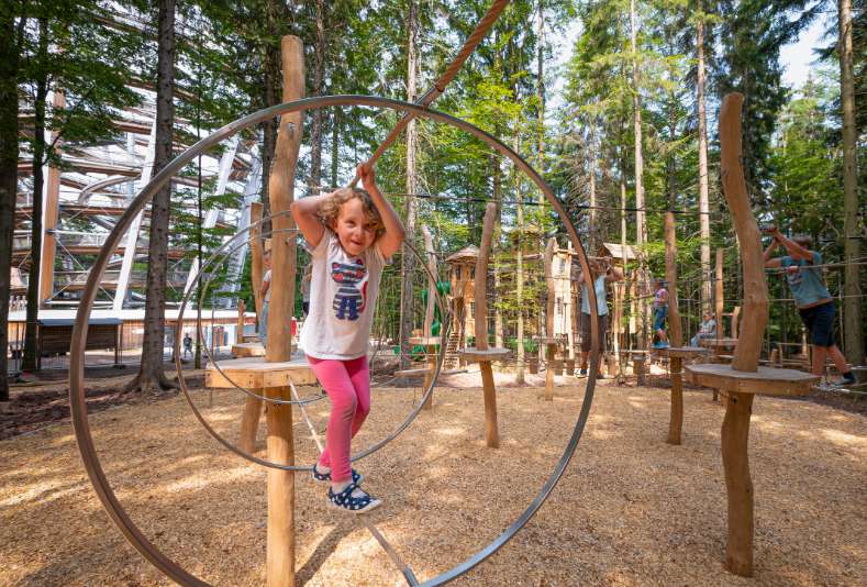 In dem perfekt in den Wald integrierten Spielplatz Abenteuerwald bewältigt ein Mädchen den Niederseilgarten