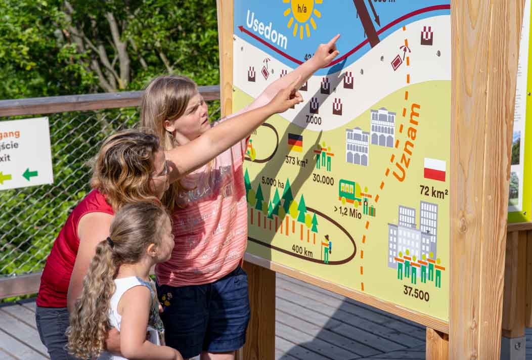 Eine Familie mit Kindern steht vor einer Lernstation und informiert sich zur Insel Usedom.