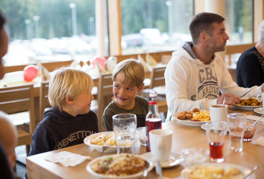 Vater sitzt mit seinen Kindern vor reichhaltig gedecktem Tisch im Restaurant des Baumwipfelpfads.